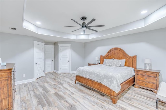 bedroom featuring ceiling fan, light wood-type flooring, and a tray ceiling