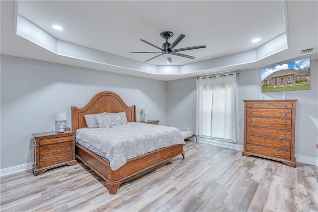 bedroom featuring light hardwood / wood-style flooring, a raised ceiling, and ceiling fan