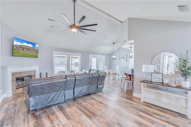 living room featuring ceiling fan, wood-type flooring, a tiled fireplace, and high vaulted ceiling