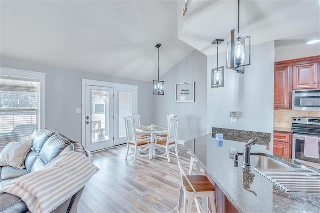 kitchen with sink, tasteful backsplash, vaulted ceiling, hanging light fixtures, and stainless steel appliances