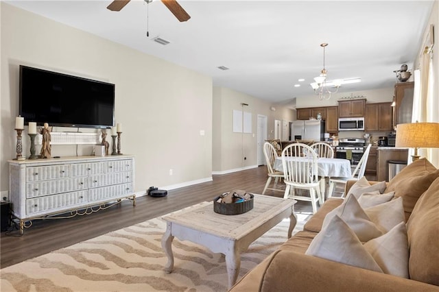 living room with ceiling fan with notable chandelier and dark wood-type flooring