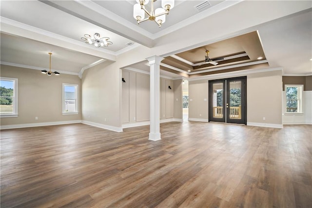 unfurnished living room with wood-type flooring, decorative columns, a healthy amount of sunlight, a raised ceiling, and french doors