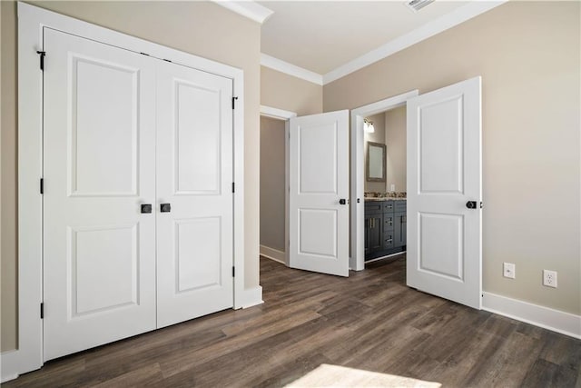 unfurnished bedroom featuring connected bathroom, a closet, crown molding, and dark wood-type flooring