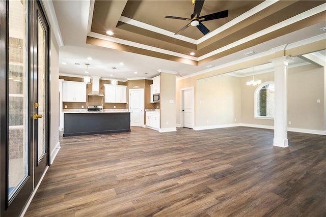 unfurnished living room with a tray ceiling, ornate columns, dark hardwood / wood-style floors, and ceiling fan with notable chandelier