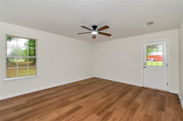 empty room featuring visible vents, a ceiling fan, wood finished floors, and a textured ceiling