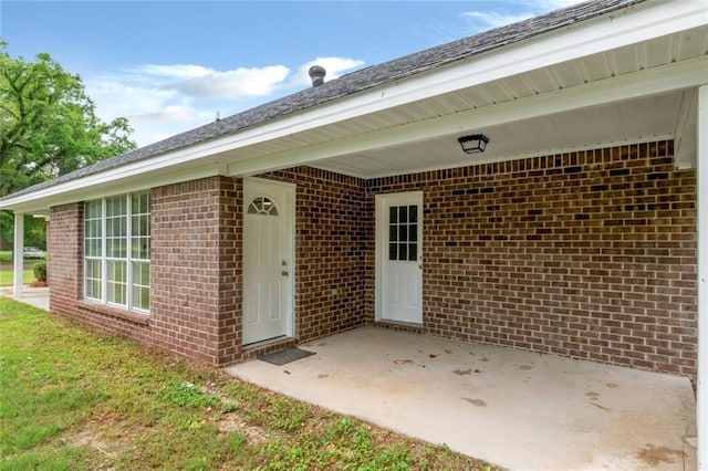 view of exterior entry featuring a patio and brick siding