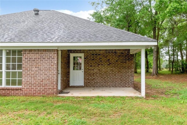 doorway to property with brick siding, roof with shingles, and a lawn