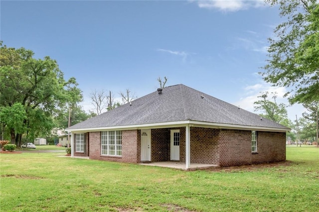 rear view of property featuring brick siding, a shingled roof, a patio area, and a lawn