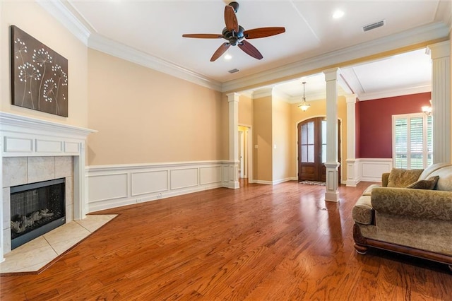 living room with light hardwood / wood-style floors, a tiled fireplace, ornate columns, ceiling fan, and ornamental molding