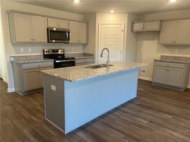 kitchen with a sink, gray cabinetry, stainless steel appliances, dark wood-style floors, and a kitchen island with sink
