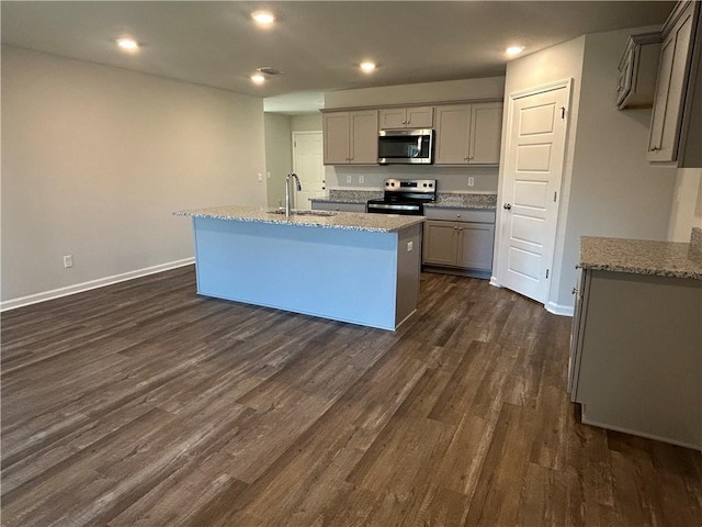 kitchen featuring appliances with stainless steel finishes, dark hardwood / wood-style flooring, light stone counters, gray cabinetry, and an island with sink