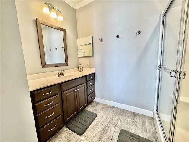 bathroom with a stall shower, ornamental molding, wood finished floors, baseboards, and vanity