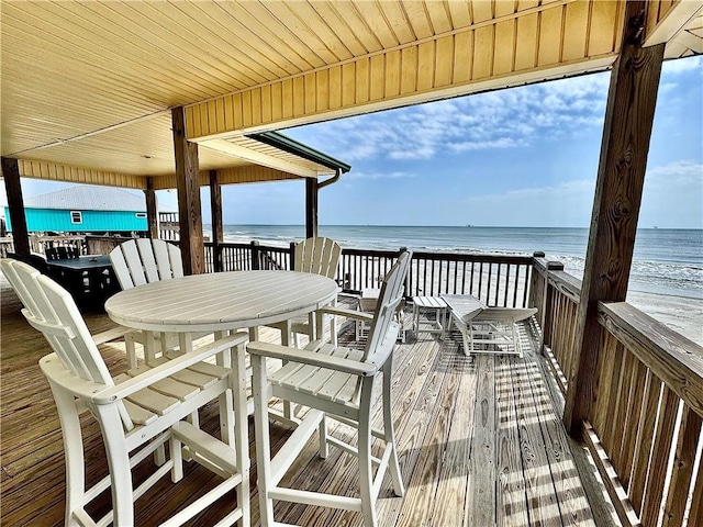 deck featuring outdoor dining area, a water view, and a beach view