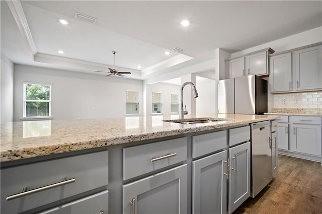 kitchen featuring a sink, gray cabinets, a raised ceiling, dark wood-type flooring, and appliances with stainless steel finishes