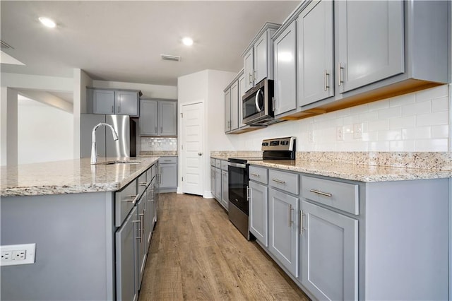 kitchen with gray cabinets, tasteful backsplash, visible vents, appliances with stainless steel finishes, and wood finished floors