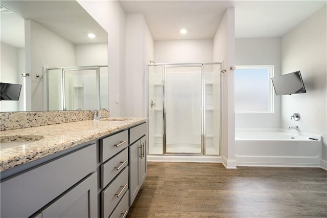 bathroom featuring wood finished floors, a shower stall, a garden tub, and double vanity