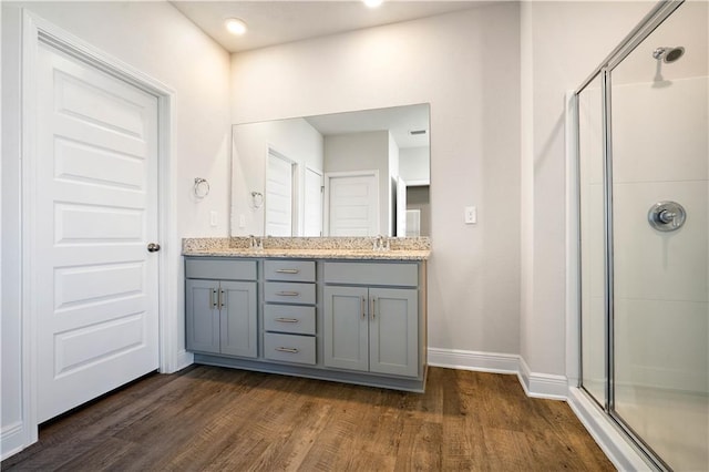 bathroom with double vanity, a sink, a shower stall, and wood finished floors