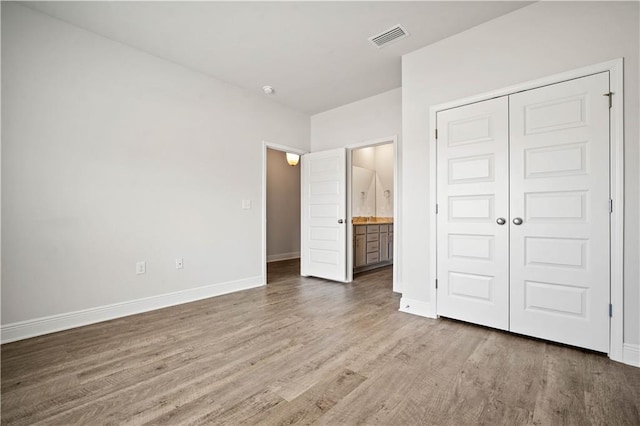 unfurnished bedroom with visible vents, a closet, baseboards, wood finished floors, and ensuite bath