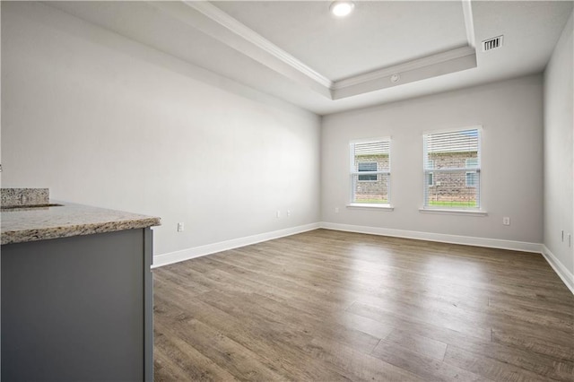 spare room with ornamental molding, baseboards, visible vents, dark wood-type flooring, and a tray ceiling