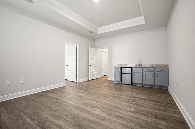 bar featuring refrigerator, ornamental molding, wet bar, dark wood-style floors, and a tray ceiling