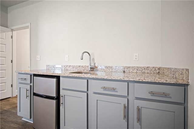 kitchen with a sink, gray cabinetry, freestanding refrigerator, light stone countertops, and dark wood finished floors