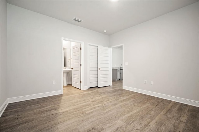 unfurnished bedroom with ensuite bathroom, visible vents, wood finished floors, and baseboards