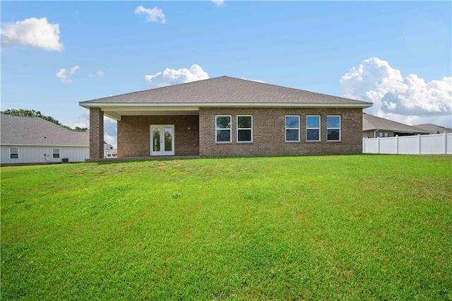 rear view of property with a lawn, brick siding, french doors, and fence