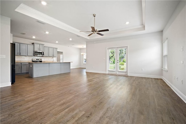 unfurnished living room featuring dark wood finished floors, a raised ceiling, ceiling fan, and ornamental molding