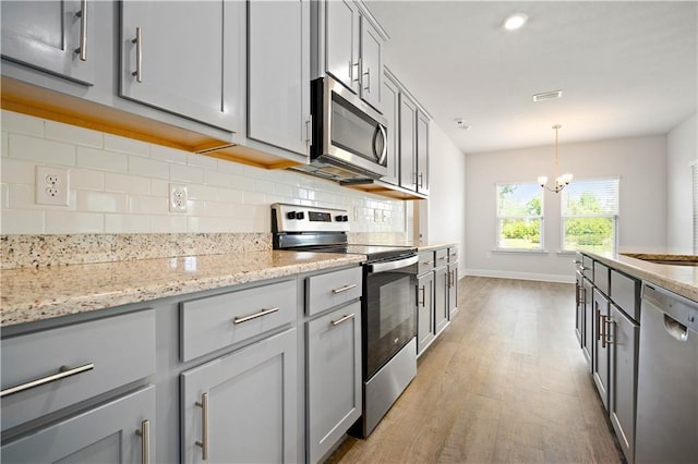 kitchen with a notable chandelier, tasteful backsplash, stainless steel appliances, and light wood-type flooring