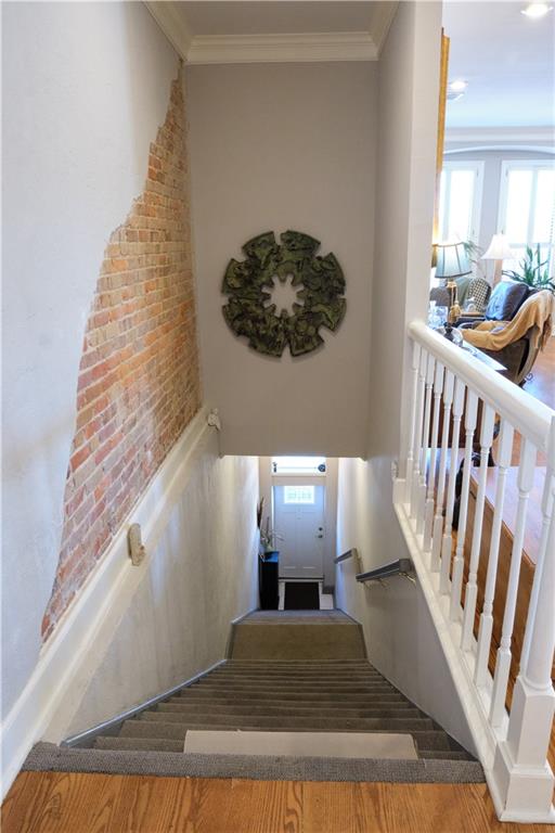 stairway with brick wall, crown molding, and dark hardwood / wood-style floors