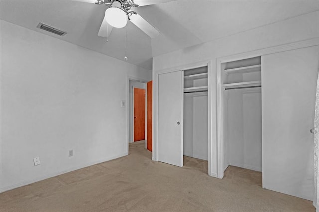 unfurnished bedroom with light colored carpet, ceiling fan, and two closets