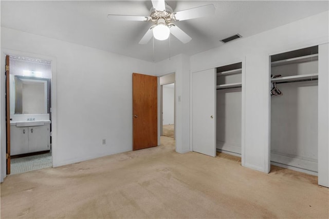 unfurnished bedroom featuring ceiling fan, light colored carpet, connected bathroom, and multiple closets