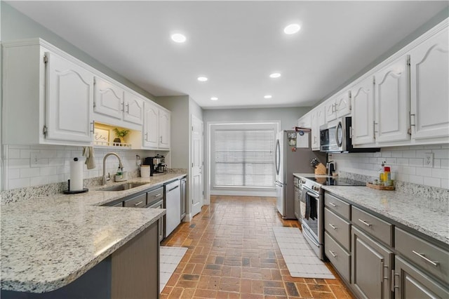 kitchen featuring white cabinetry, sink, light stone countertops, stainless steel appliances, and backsplash