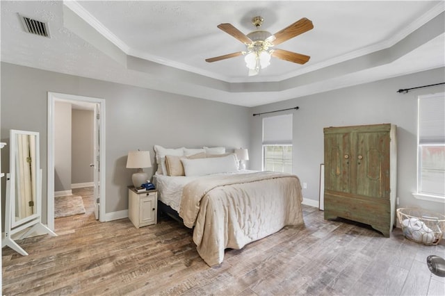 bedroom featuring a raised ceiling, ceiling fan, light hardwood / wood-style flooring, and crown molding