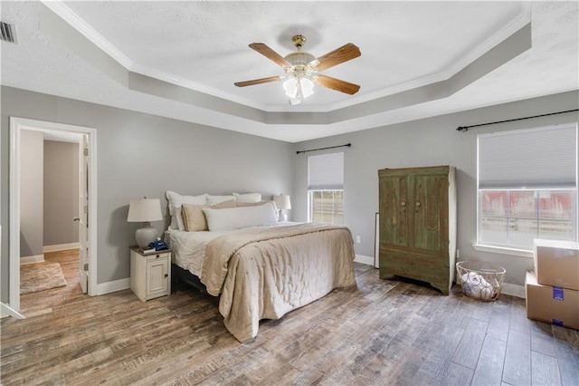 bedroom featuring ceiling fan, a raised ceiling, wood-type flooring, and crown molding