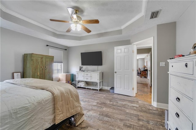 bedroom with wood-type flooring, a tray ceiling, ceiling fan, and ornamental molding