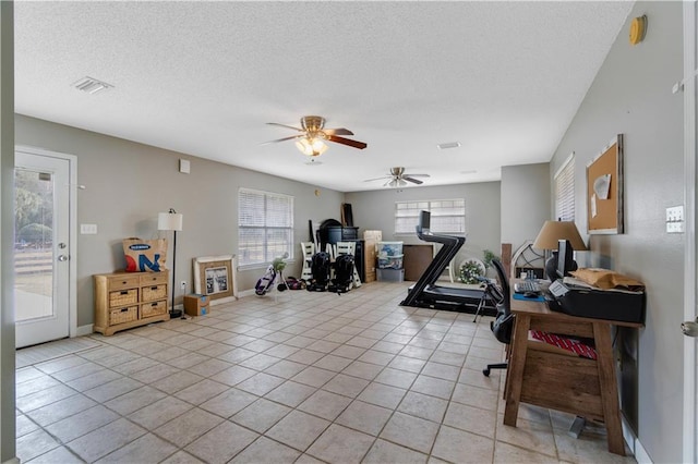 exercise room featuring ceiling fan, light tile patterned floors, and a textured ceiling