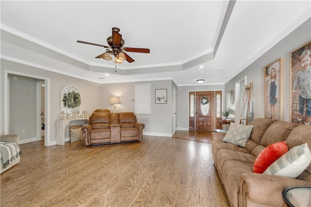 living room with light hardwood / wood-style floors, a tray ceiling, ornamental molding, and ceiling fan