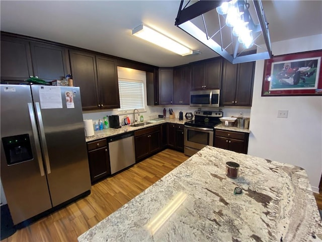 kitchen featuring dark brown cabinets, light stone counters, light wood finished floors, a sink, and appliances with stainless steel finishes