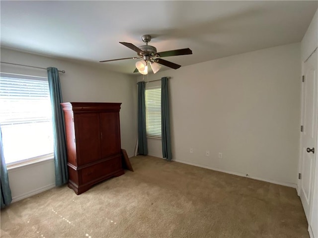 unfurnished bedroom with light carpet, baseboards, a ceiling fan, and multiple windows