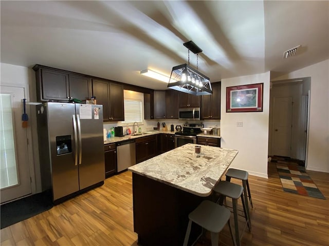 kitchen featuring dark brown cabinets, wood finished floors, a kitchen bar, a sink, and appliances with stainless steel finishes