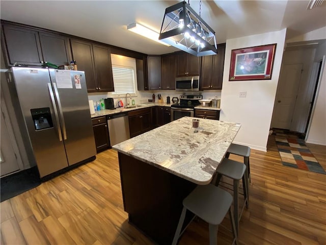 kitchen featuring a kitchen bar, a sink, dark brown cabinetry, light wood-type flooring, and appliances with stainless steel finishes
