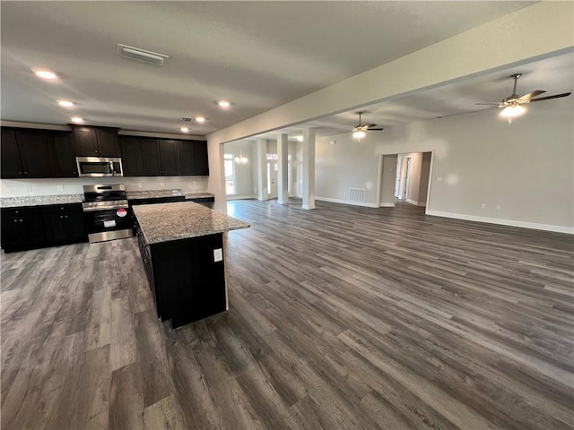 kitchen with dark wood-type flooring, ceiling fan, appliances with stainless steel finishes, light stone counters, and a kitchen island