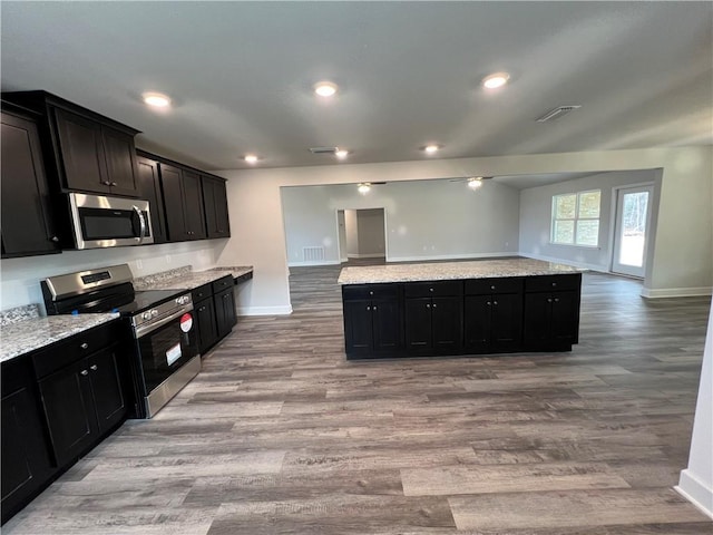 kitchen with stainless steel appliances, light stone countertops, and light wood-type flooring