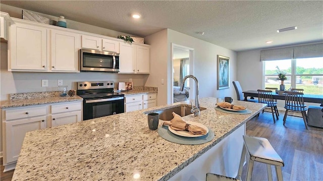 kitchen with sink, white cabinets, a textured ceiling, light stone counters, and appliances with stainless steel finishes