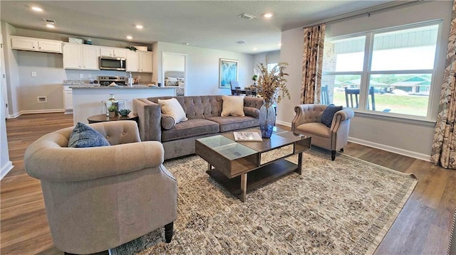 living area with baseboards, visible vents, wood finished floors, and recessed lighting