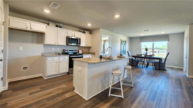 kitchen with appliances with stainless steel finishes, dark wood-style flooring, white cabinets, and an island with sink