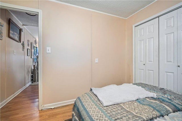 bedroom with a closet, hardwood / wood-style floors, a textured ceiling, and crown molding