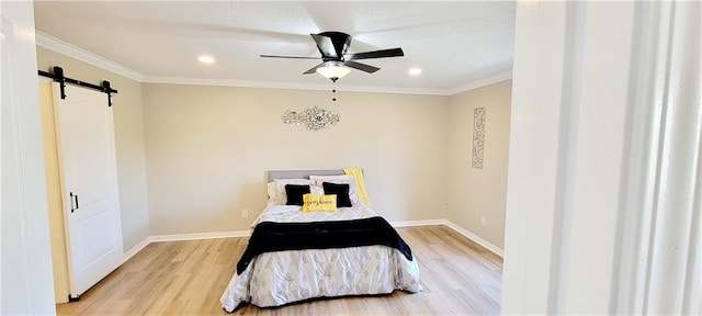 bedroom with crown molding, a barn door, light hardwood / wood-style floors, and ceiling fan