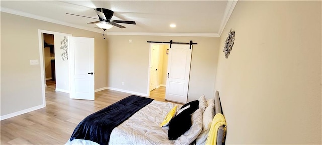 bedroom with ornamental molding, a barn door, light wood-type flooring, and ceiling fan